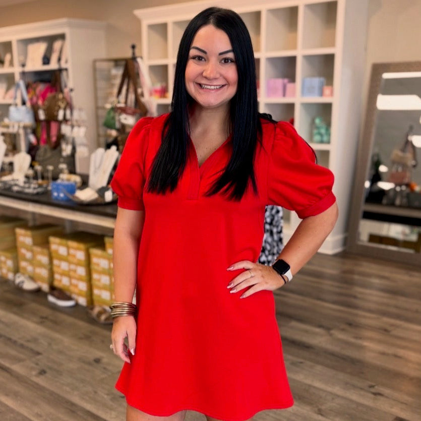 Woman in a red dress standing in a store with wooden flooring.