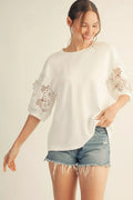 Woman wearing a white blouse with lace sleeves and denim shorts on a plain background