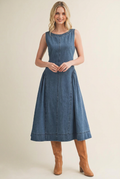 Model wearing a sleeveless flared denim midi dress with tan knee-high boots and no hat